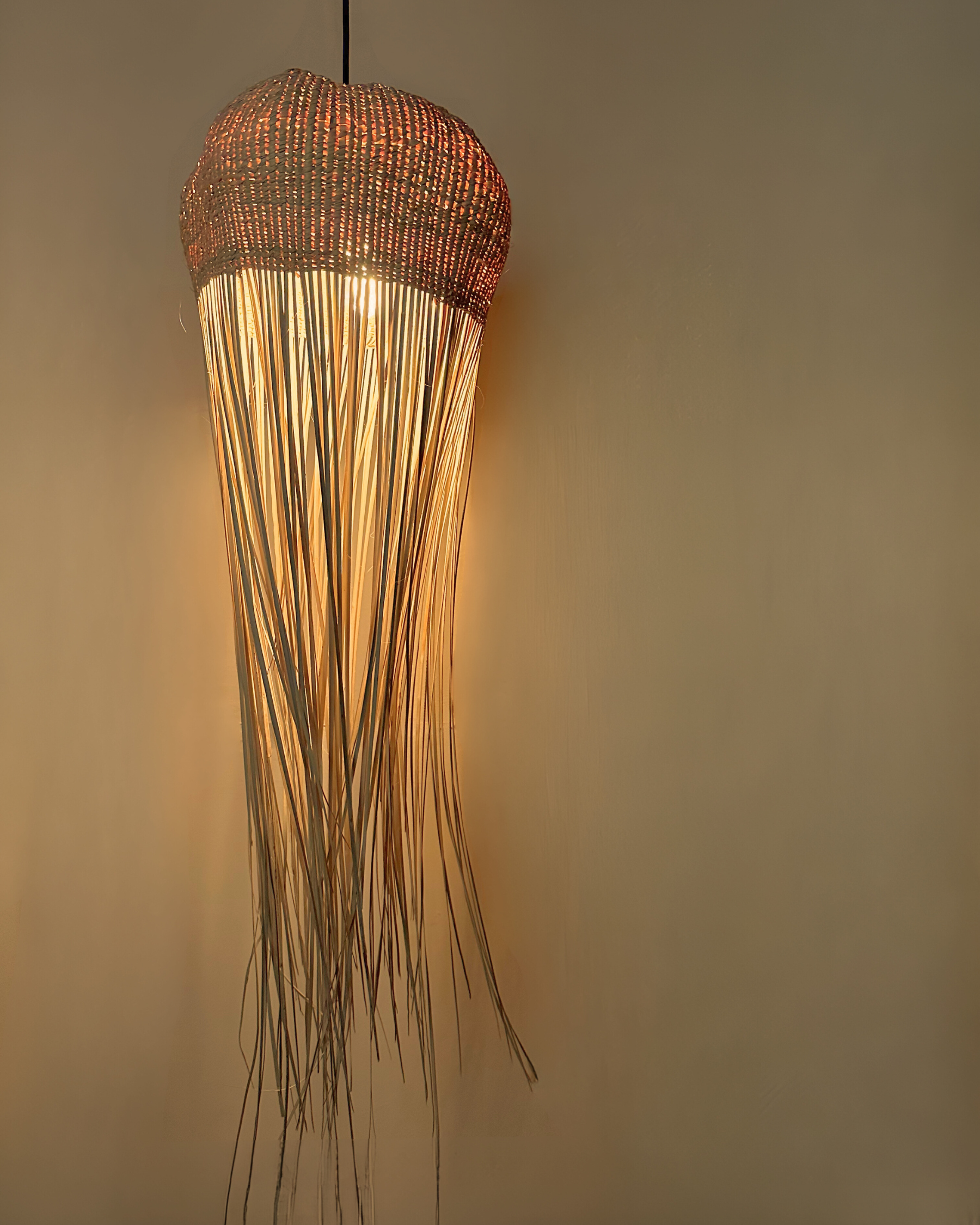 Tall jellyfish-inspired pendant light with woven top and flowing raffia strands, handmade and customisable lighting