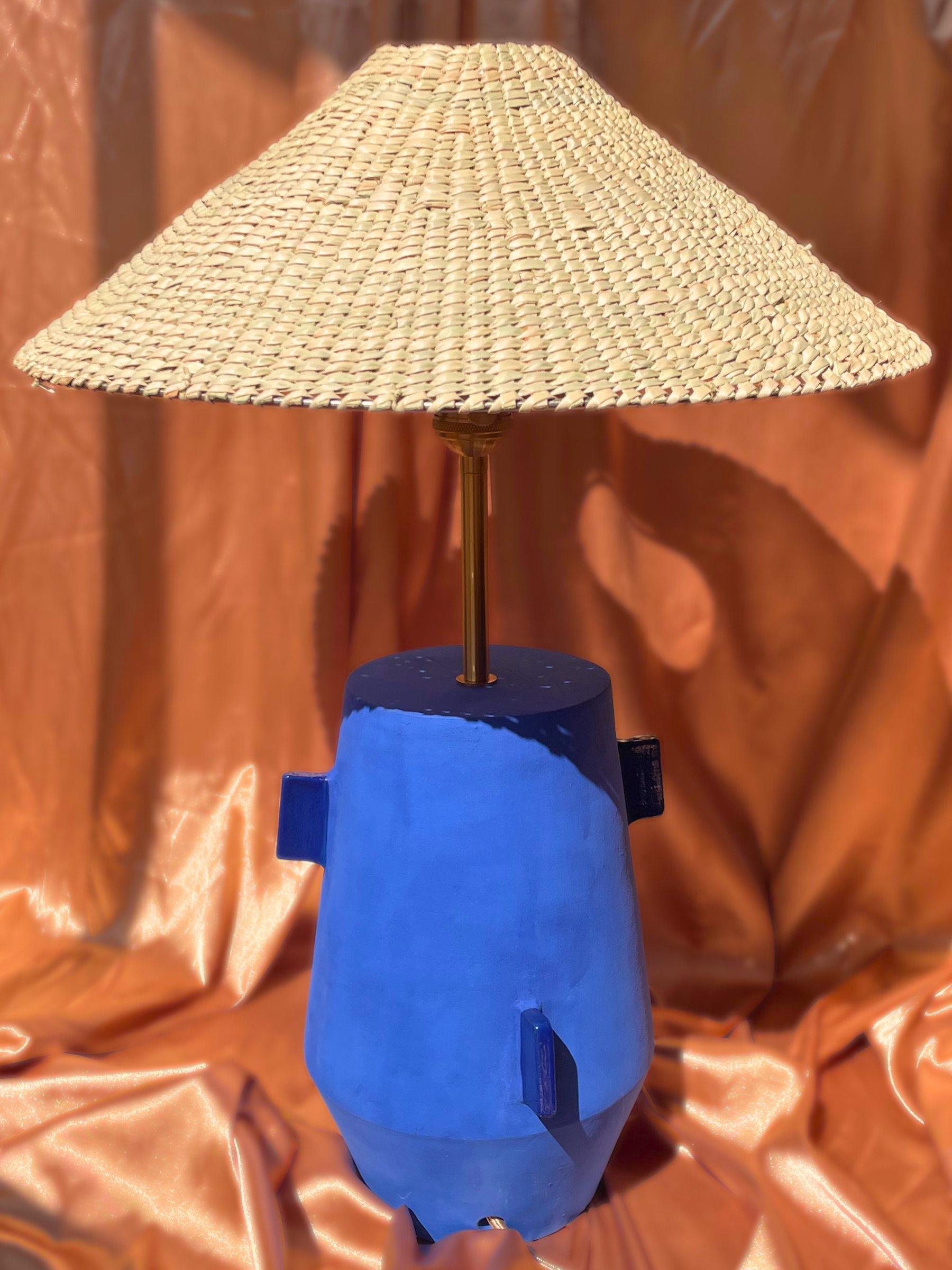 Ceramic handmade table lamp with a blue base and woven lampshade on an orange background