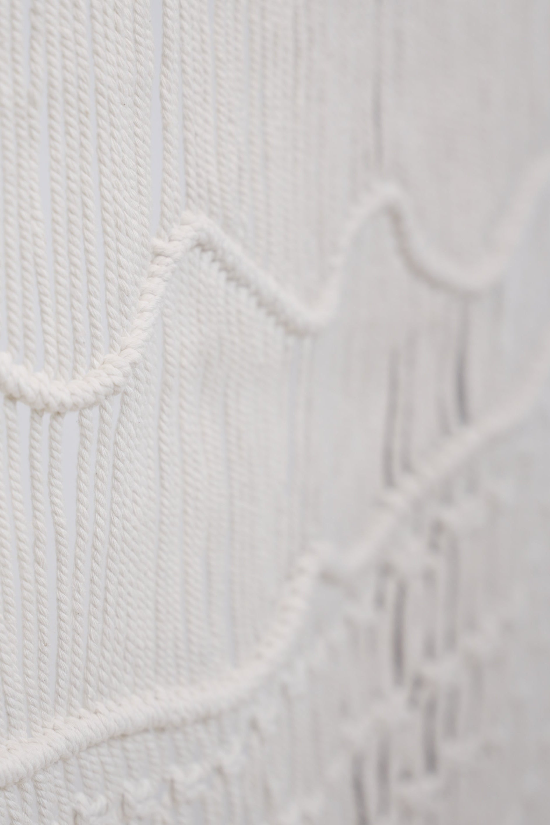 Close-up of the Macrame wall hanger hand woven with crisp white macrame on a one of a kind wooden rod