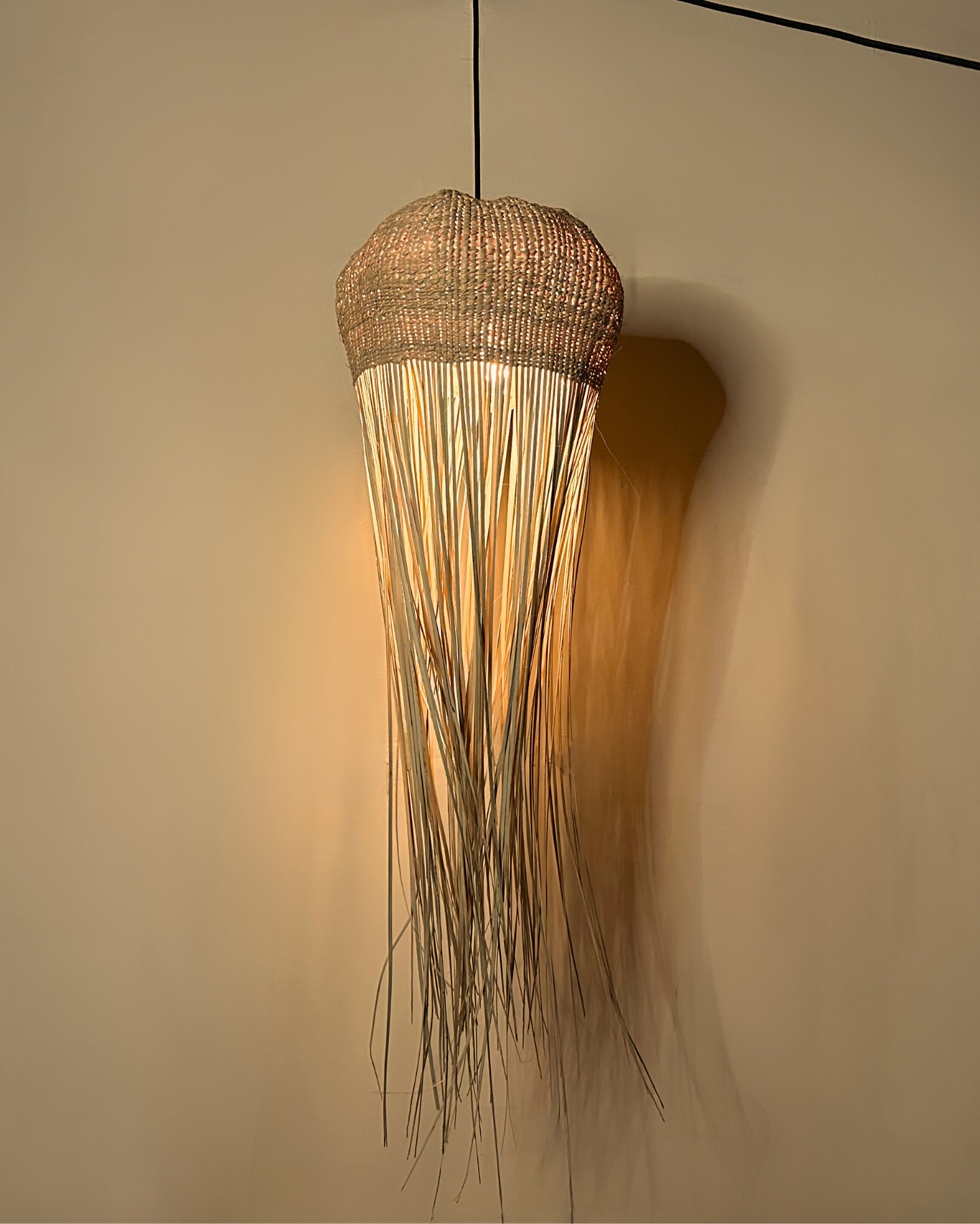 Tall jellyfish-inspired pendant light with woven top and flowing raffia strands, handmade and customisable lighting
