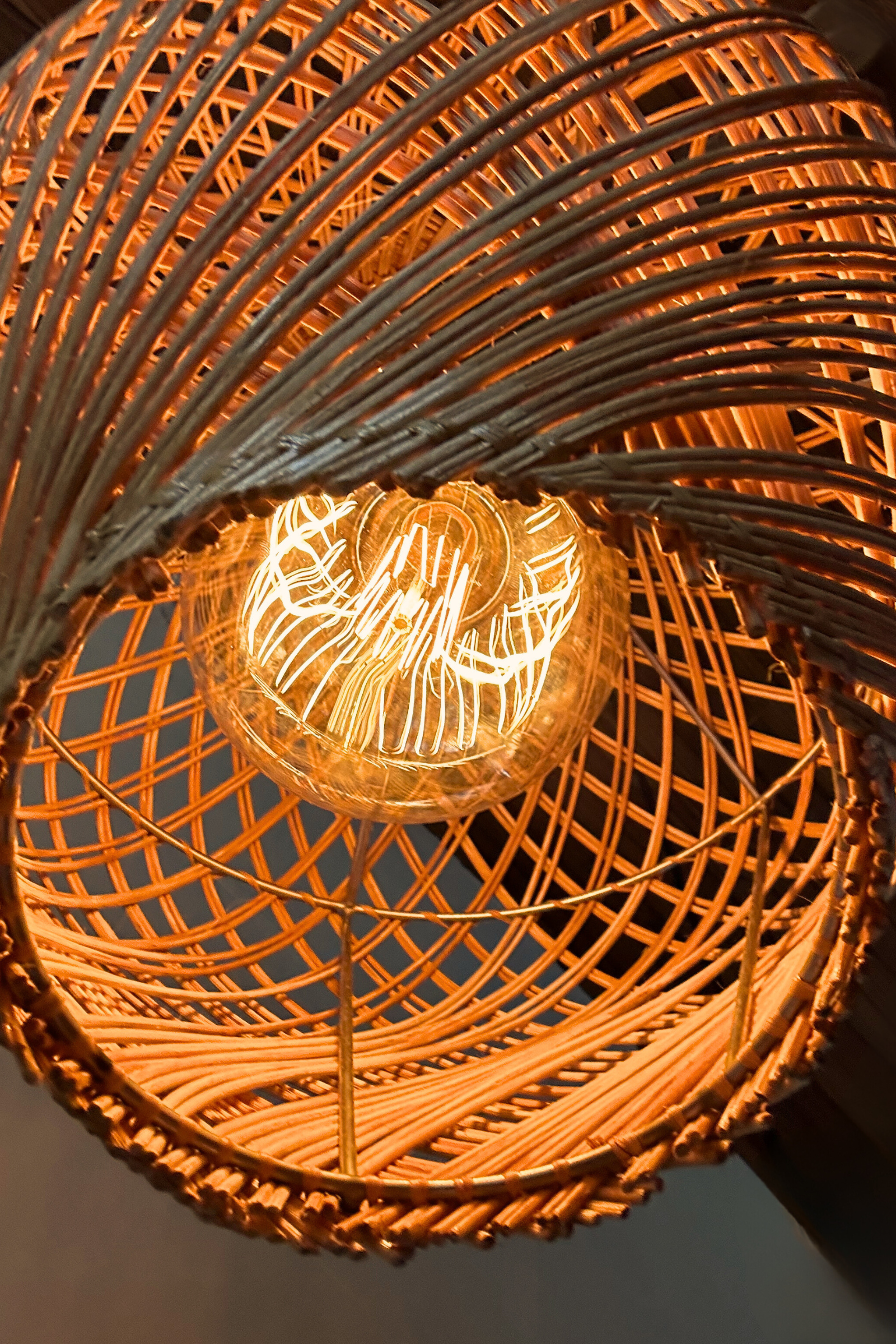Locally handwoven rattan pendant light with a warm glow, from below