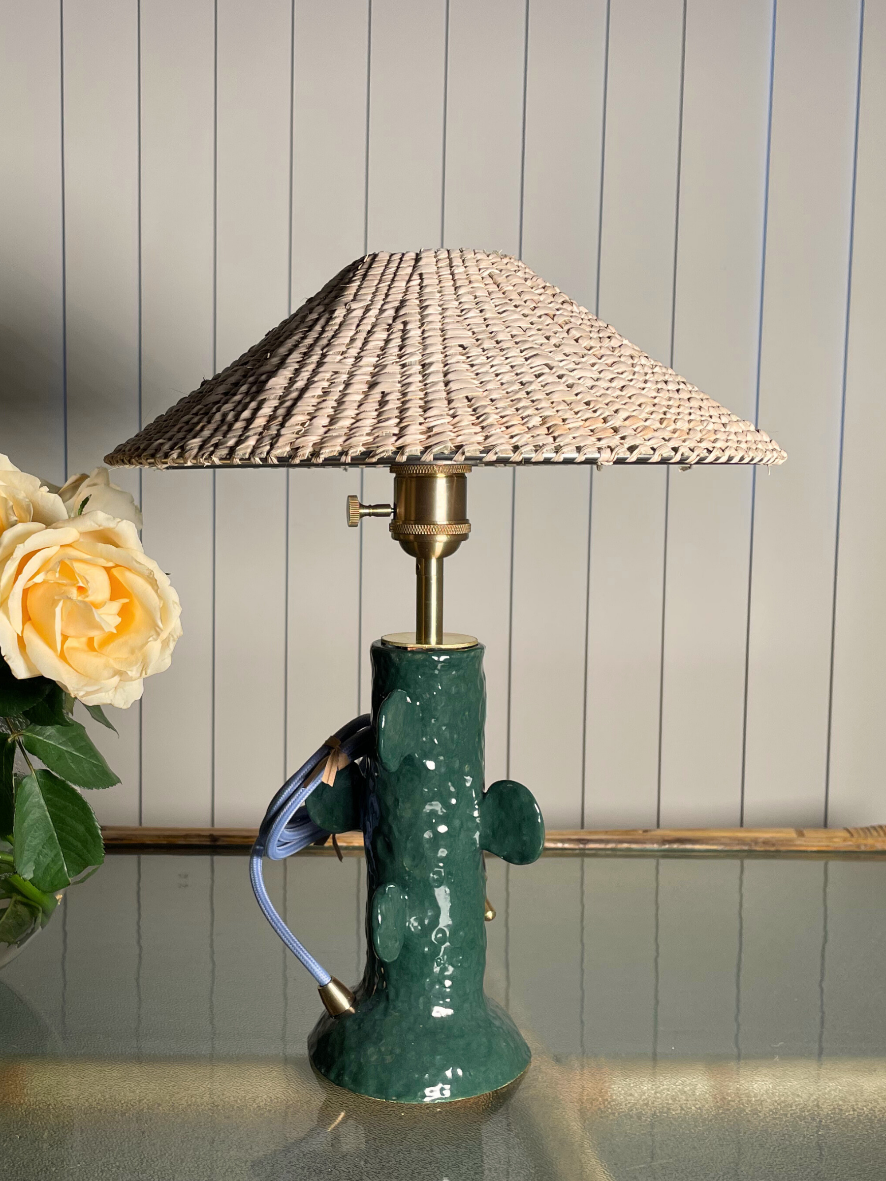 Table lamp with green base and woven shade on a wooden surface