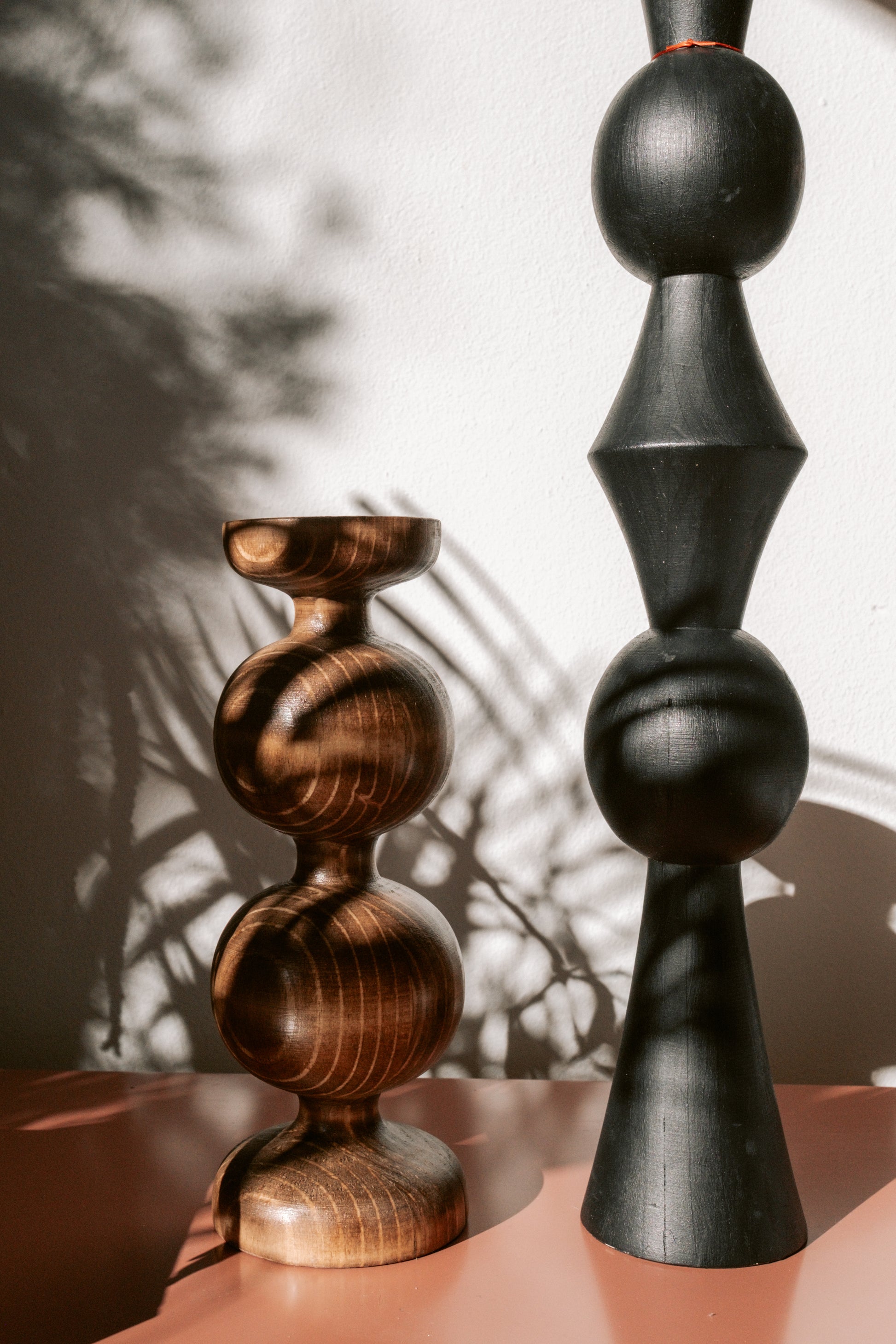 Two wooden sculptures, one brown and one black, on a surface with a blurred background.