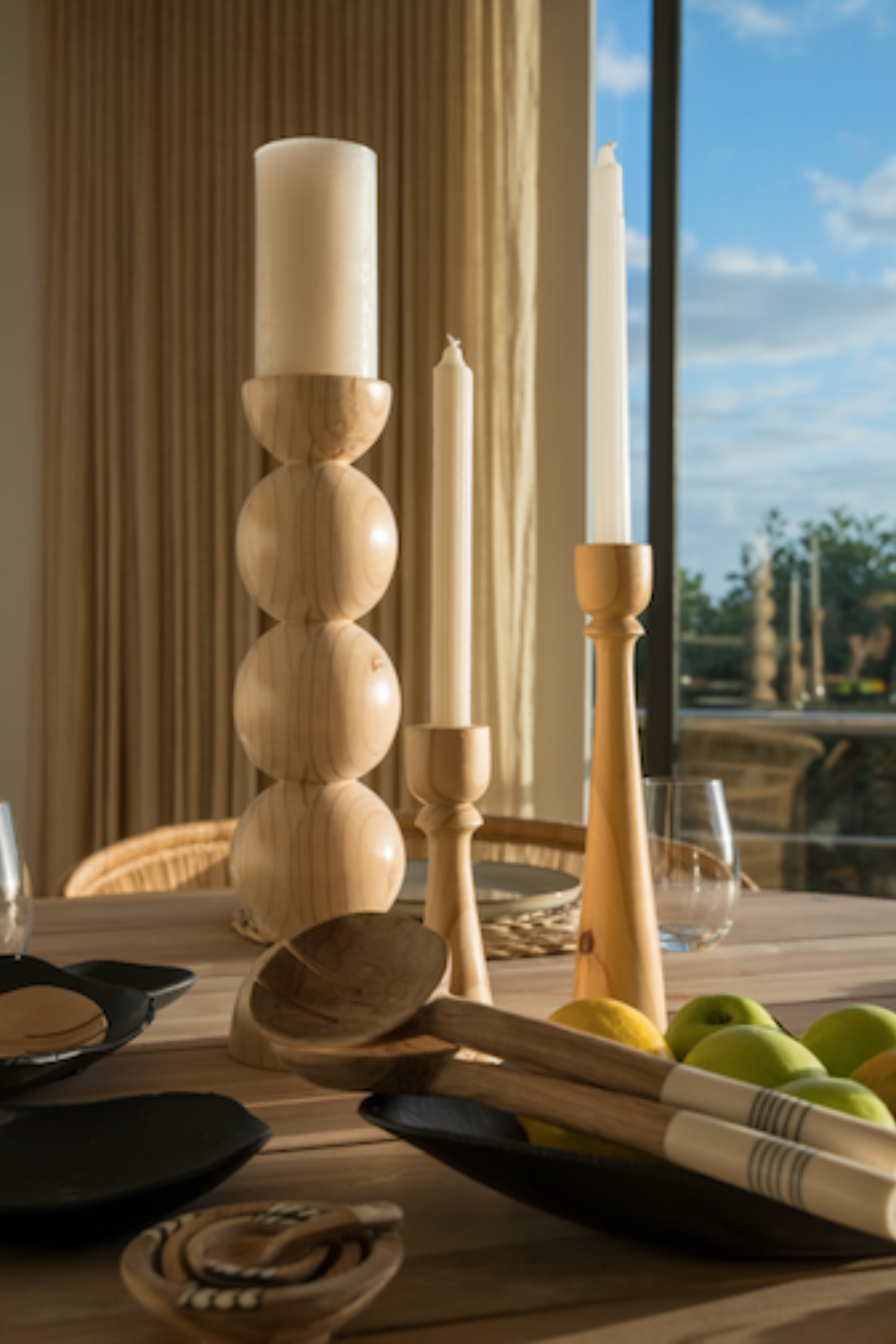 Wooden candle holders and spoons on a table with a scenic view outside.
