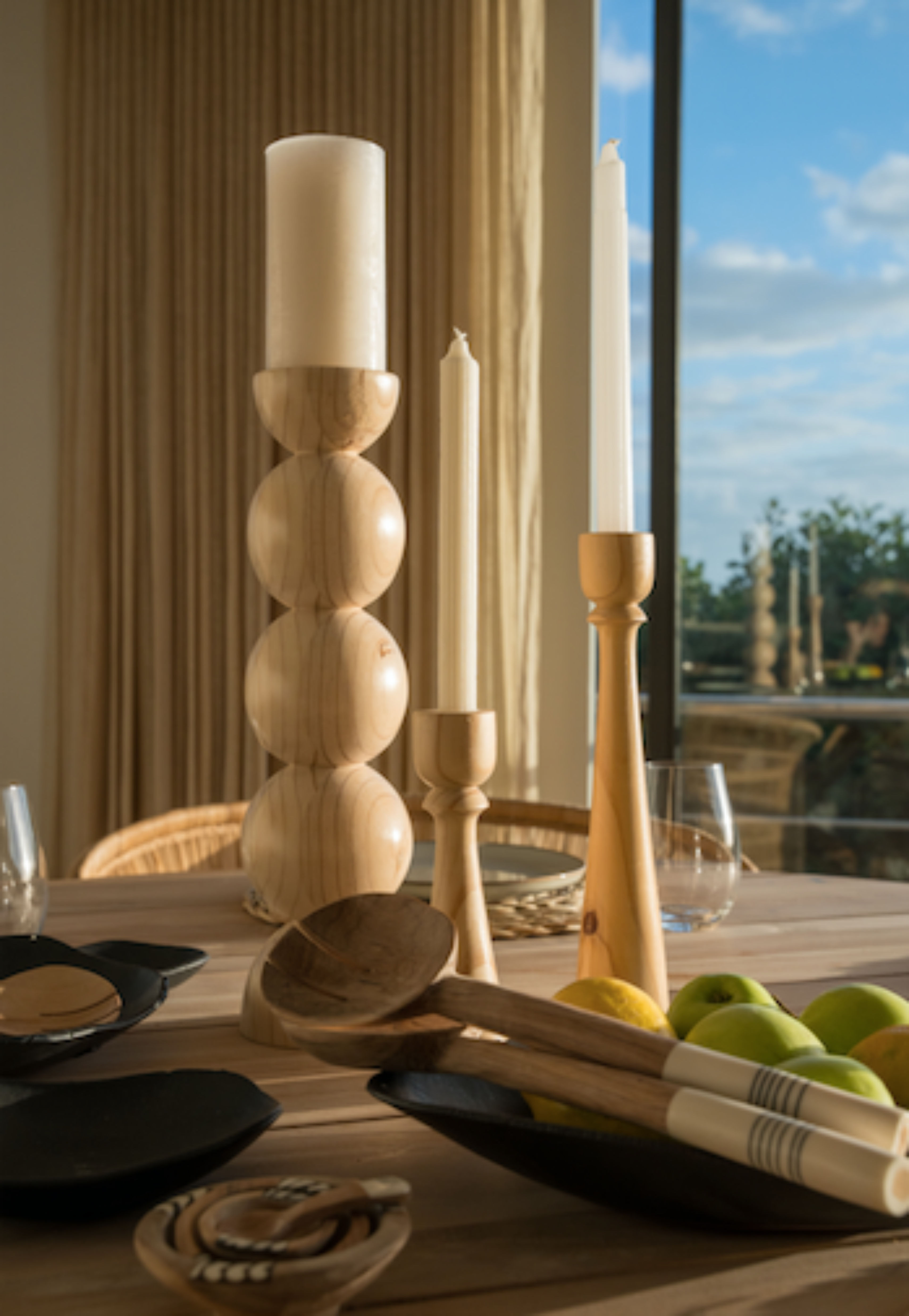 Wooden candle holders and spoons on a table with a scenic view outside.