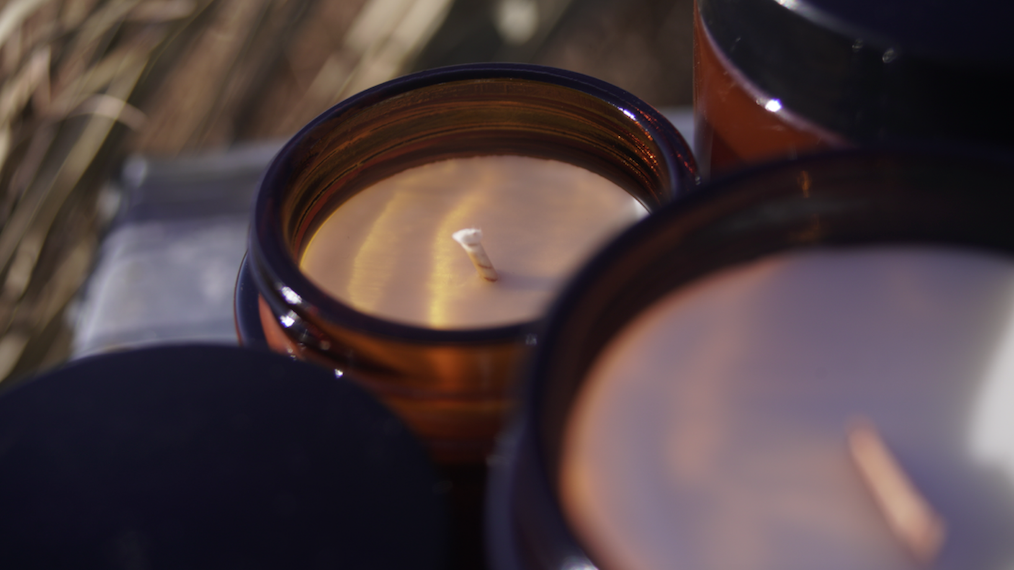 Close-up of unlit soy candles in amber glass jars with cotton wicks 